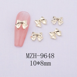 Macro detail of gold bow-shaped alloy nail art charms size 10x8mm on pink display