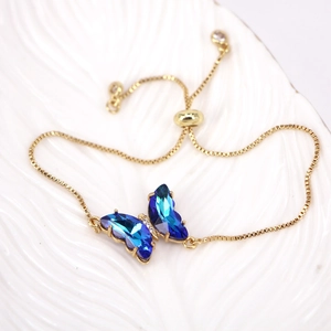 Detailed macro view of a gold chain bracelet with a blue gradient crystal butterfly pendant