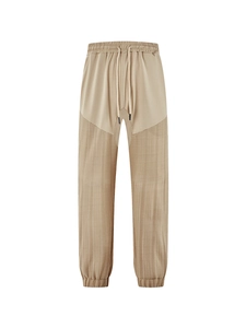 Detail of beige drawstring joggers showing patchwork design and vertical pleated texture