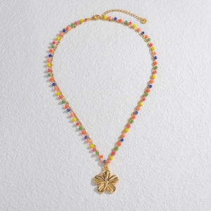 Detailed macro of gold beaded necklace with colorful beads and flower pendant on white wall