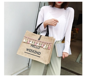Close-up of jute tote bag featuring Hello Weekend print and colorful tassel accents