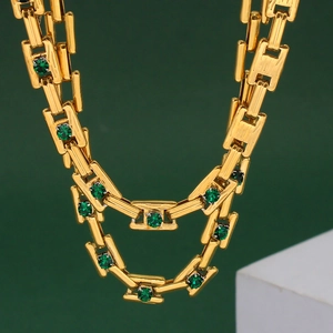 Macro detail of golden geometric chain necklace featuring green round cut gemstone accents