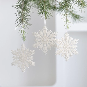 Set of three white glitter snowflake Christmas ornaments hanging on a green pine branch