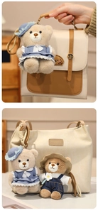 Close-up of cute plush bear charms in blue lace dress and denim overalls on beige handbags