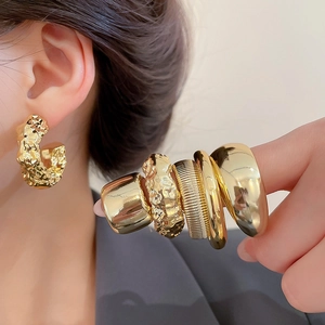Detail of chunky gold geometric earrings and matching rings on model for a luxe look