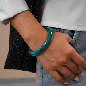Detail view of a cyan marble texture acrylic bangle worn on a wrist with casual outfit