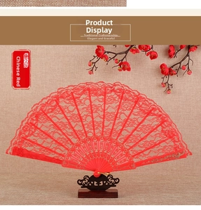 Detail of red lace folding fan with gold patterns on a beige textured background
