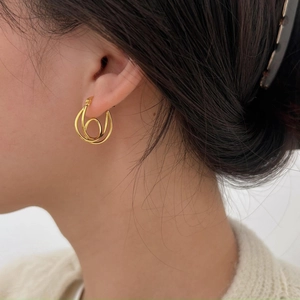 Macro shot of minimalist gold knotted hoop earring on ear with polished metal finish