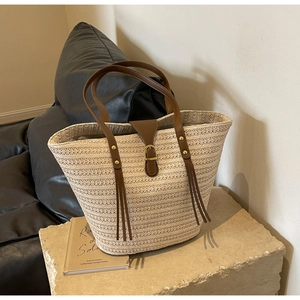 Detail of beige straw tote bag with brown leather handles on a stone pedestal