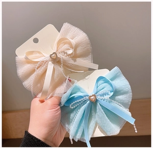 Macro detail of sweet chiffon bow hair clips with pearl heart centers on display cards