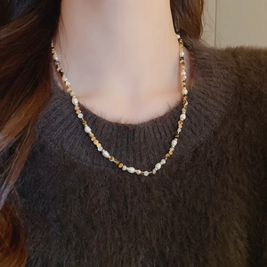 Close-up of pearl and agate beaded necklace on a brown knit sweater for vintage style