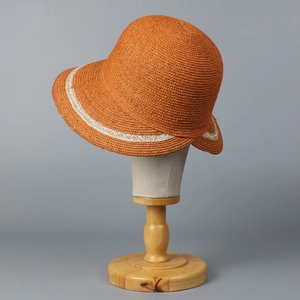 Detailed texture of orange woven straw sun hat with decorative beige band on display head