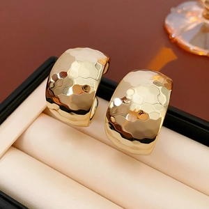 Detail of gold C-shaped earrings with hammered texture displayed in a luxury jewelry box