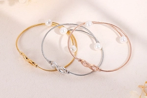 Detail van stalen gevlochten armbanden met infinity symbolen en witte parels in goud