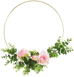 Close-up of a golden metal hoop wreath featuring pink silk roses and green eucalyptus leaves