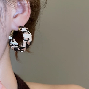 Macro shot of C-shaped leopard print leather earrings worn by a model in soft lighting