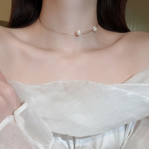 Close-up of elegant gold neck ring with twin white pearl pendants on model collarbone