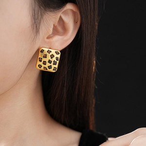 Close-up of square gold leopard print earring with orange gems worn by a model