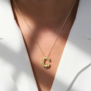 Close-up of gold bubble letter C pendant on a fine chain worn with a white blazer