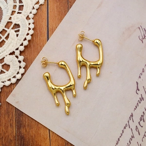 Macro shot of liquid lava textured gold earrings on vintage paper and wood background