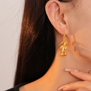 Close-up of matte gold bamboo leaf earrings with double fruit pendants on model