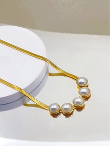 Detailed macro view of golden snake bone chain with five white pearls on a white stand