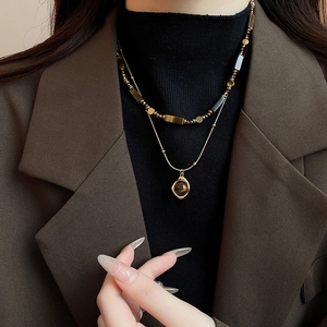 Detail of layered gold-plated tiger eye stone necklaces on a model wearing a brown blazer