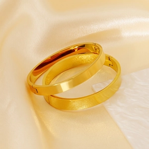 Polished 18K gold stainless steel clasp bangles displayed on luxury silk and stone