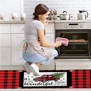 Detail of Christmas kitchen mat with red truck pattern and holiday text on a plaid border