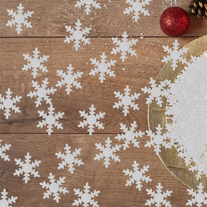 Macro detail of white glitter snowflake confetti on dark wooden table with festive ornaments