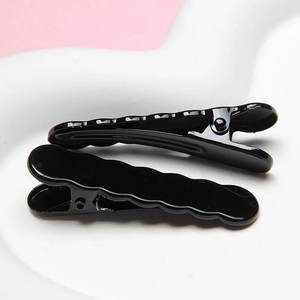 Close-up of black wave-shaped hair clips with glossy finish on a white plate