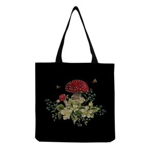 Close-up of embroidered red mushroom, flowers, and bees on black canvas tote bag