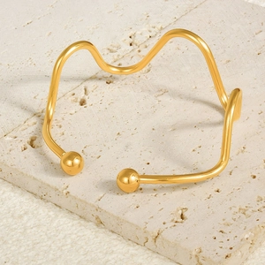 Close-up of a wavy 18k gold adjustable stainless steel bangle on a natural stone surface