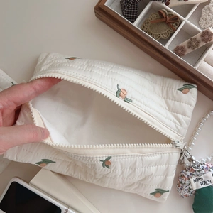 Detailed shot of quilted white makeup bag with fruit embroidery and pearl strap detail