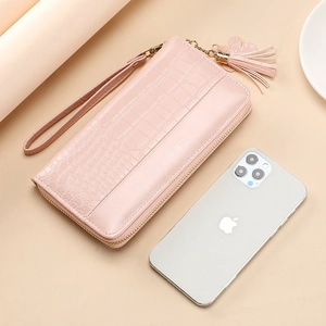 Pink crocodile pattern long wallet with wristlet and tassel, shown with a phone for scale