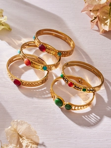 Detailed close-up of retro hollow gold bangles with colorful gemstones on white texture