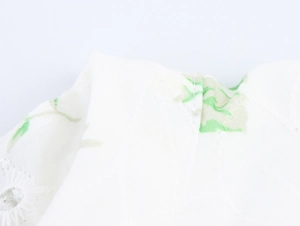 Detailed close-up of white dress fabric with green leaf print and eyelet embroidery