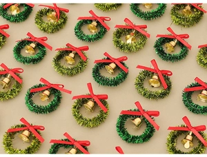 Flat lay of mini green Christmas wreaths with red bows and gold bells for DIY decor