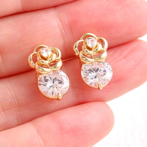 Boucles d'oreilles rose dorée avec zircons ronds présentées sur un doigt pour l'échelle