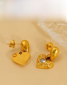 Macro detail of gold-plated heart earrings with hammered texture and sparkling zircon