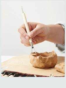 Detail of pottery sculpting tool with wooden handle carving clay during craft work