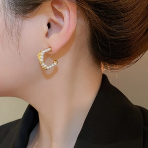Close-up of a model wearing gold C-shaped earrings with embedded white pearls