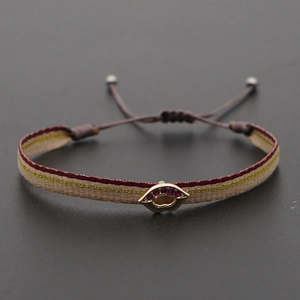 Macro shot of boho woven strap bracelet with gold lip charm and purple crystals