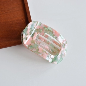 Detail of a rectangle acetate hair claw clip with pink and green marble texture