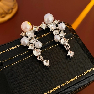Macro shot of silver leaf earrings with shimmering rhinestones and white pearls on dark box
