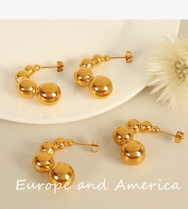 Close-up of golden bean-shaped C-style earrings with polished metallic sphere design