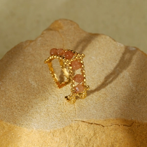 Detail of a vintage gold beaded ring with orange natural stones on a textured rock base