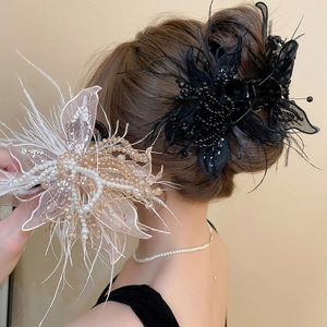 Detail view of large lace hair claws with pearls and feathers in black and champagne