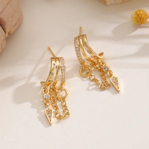 Detail of gold zircon earrings with delicate chains and geometric arrow pendants