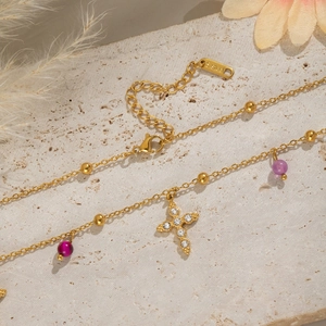 Gold stainless steel cross necklace with purple natural stones on stone background